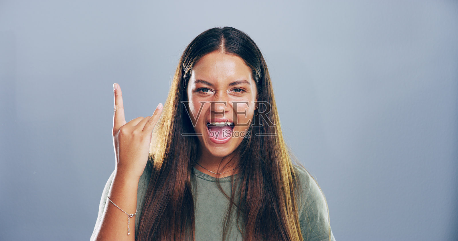 摇滚、表情符号和女性肖像在工作室中做出疯狂的手势，展现重金属和前卫的态度。模拟空间，叛逆者和做出朋克手势的人，符号和灰色背景上的魔鬼角。照片摄影图片