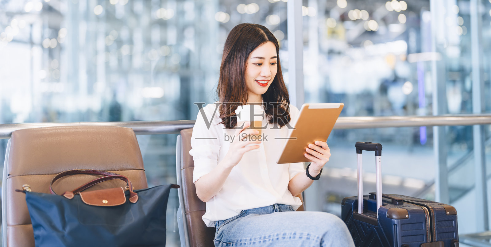 一位亚洲女性商务乘客坐在机场候机厅，旁边放着行李，准备出发进行全球旅行。照片摄影图片
