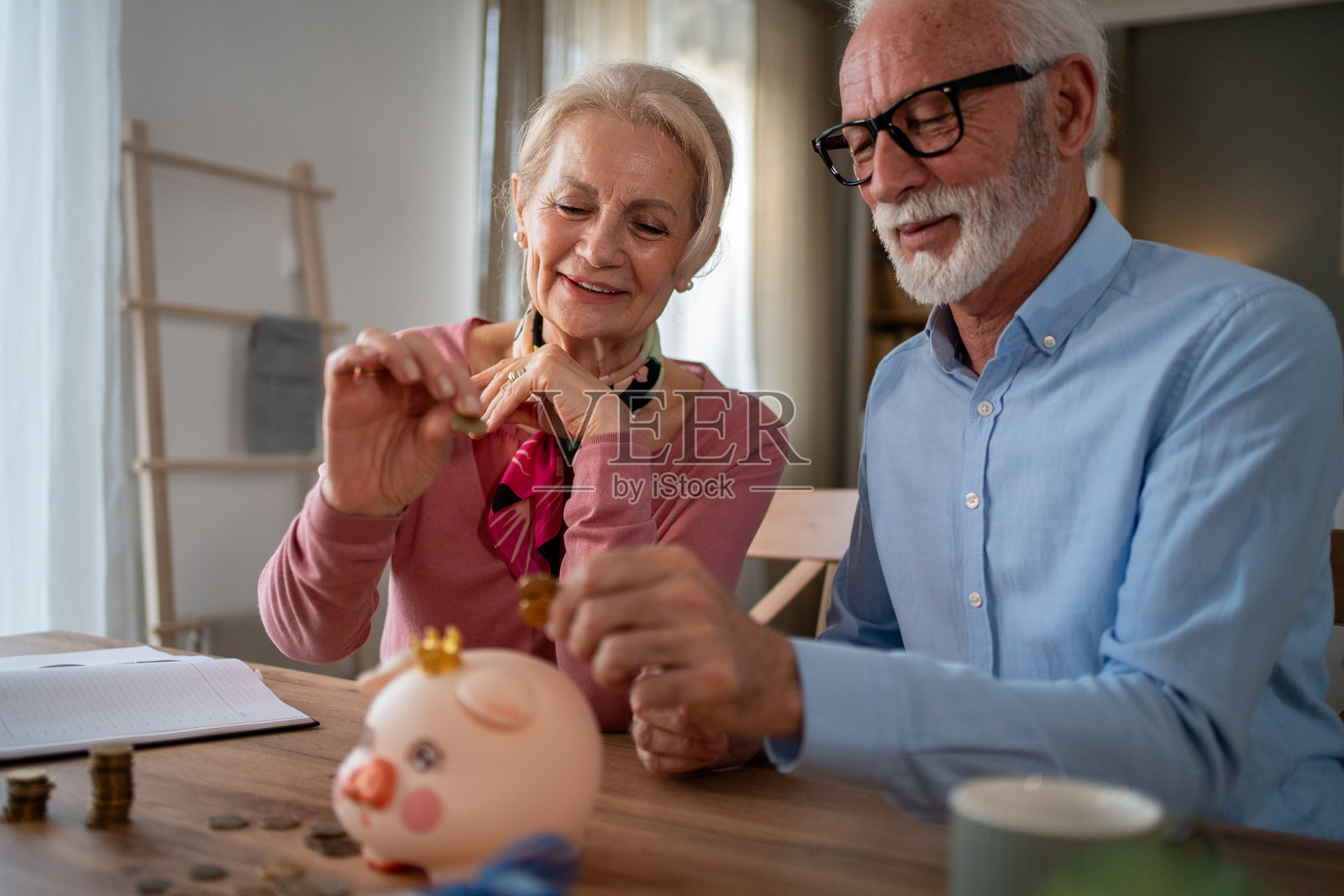 快乐的老年夫妇在家中往储蓄罐里投币照片摄影图片