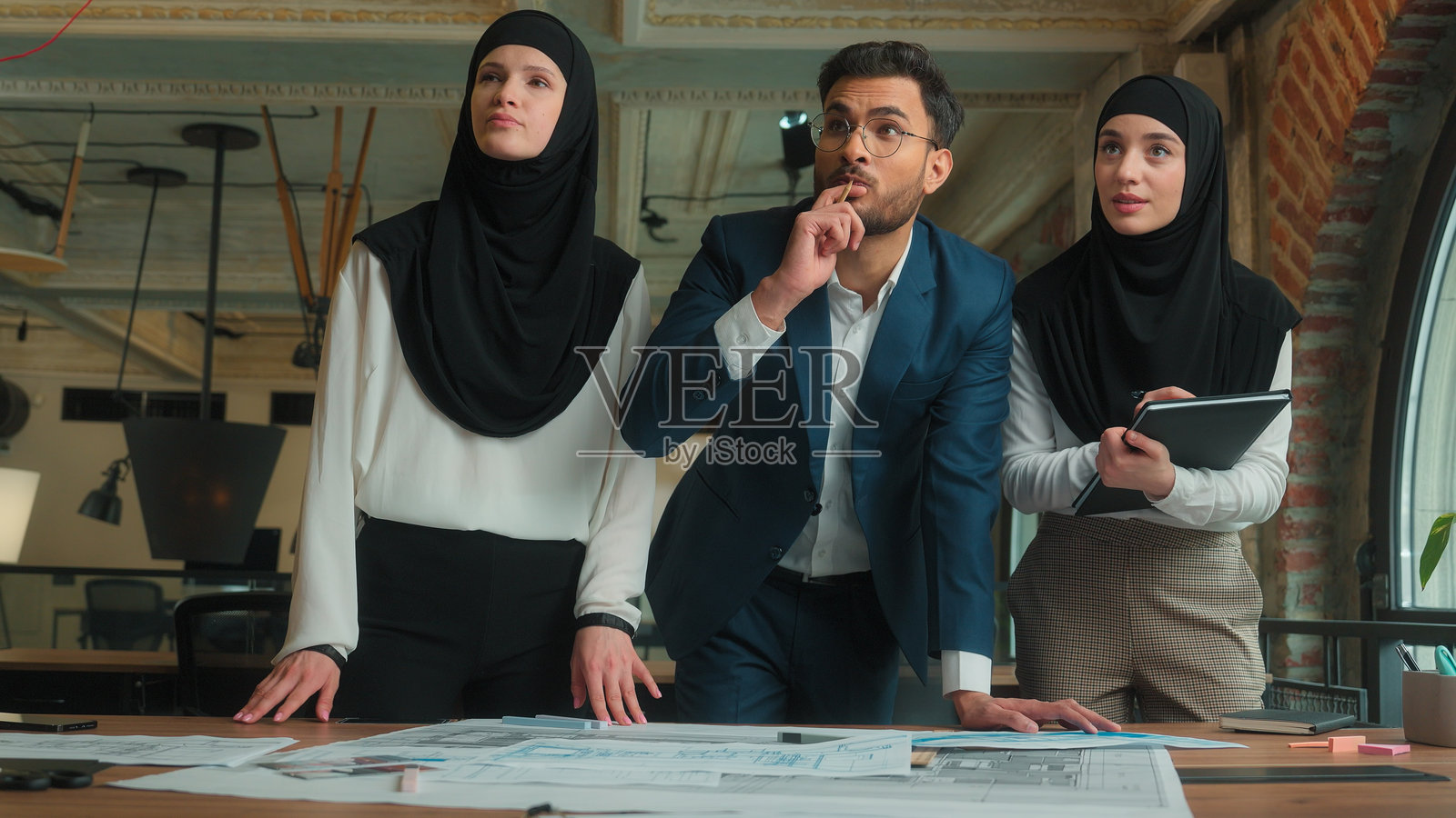 印度男性穆斯林女性戴着头巾的商业团队，建筑师、工程师、设计师和建筑工人，男女共同在桌子上绘制建筑平面图、施工蓝图草图，进行办公规划讨论。照片摄影图片