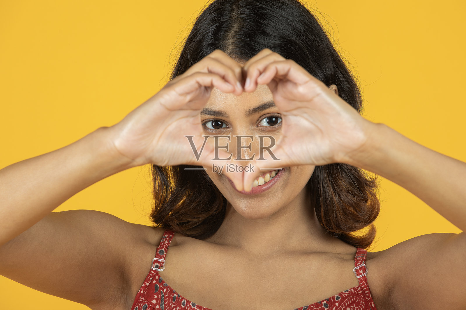 女人在黄色背景下做出心形手势的肖像照片摄影图片