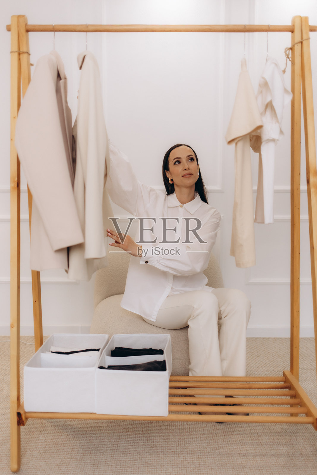 一位微笑的中年女性在明亮的衣橱房间里挑选衣服，展现了休闲购物或穿衣的场景。照片摄影图片