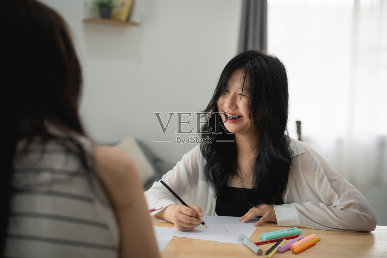 亚洲年轻女性在明亮的房间里微笑着用彩色马克笔绘画，创作艺术作品并与朋友享受创意时光。照片摄影图片