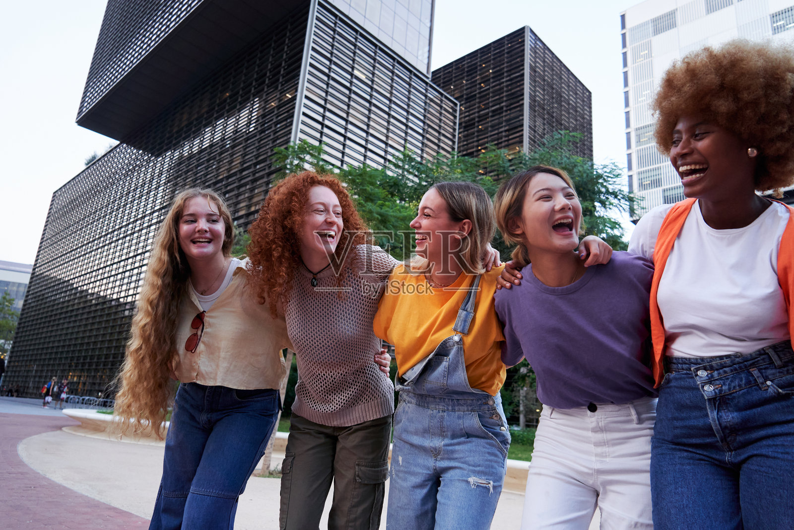 多民族的年轻女性在城市户外相拥而笑，享受着友谊。照片摄影图片