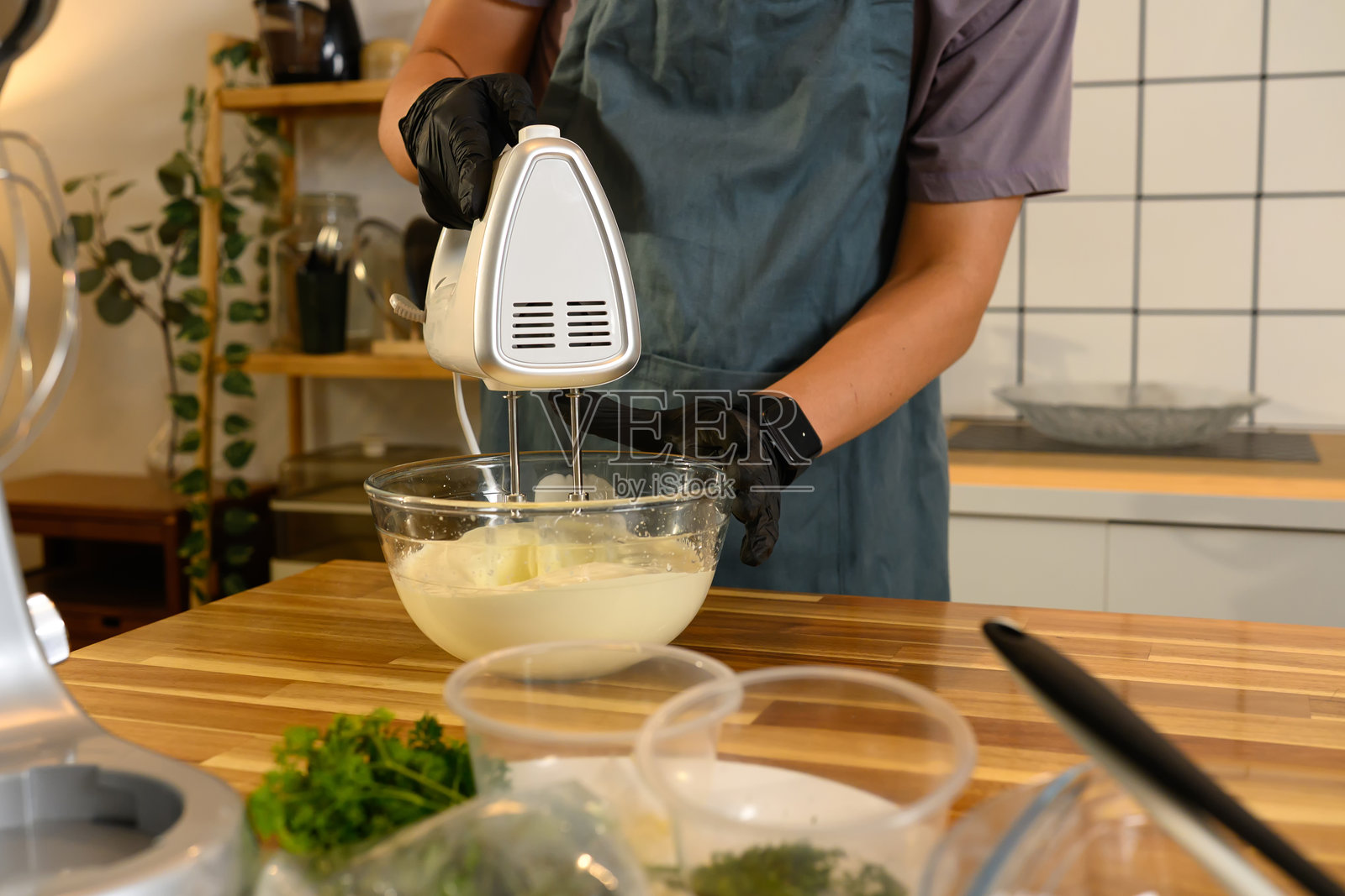 戴着黑手套的男子用电动手持搅拌器在透明玻璃碗中搅拌奶油照片摄影图片