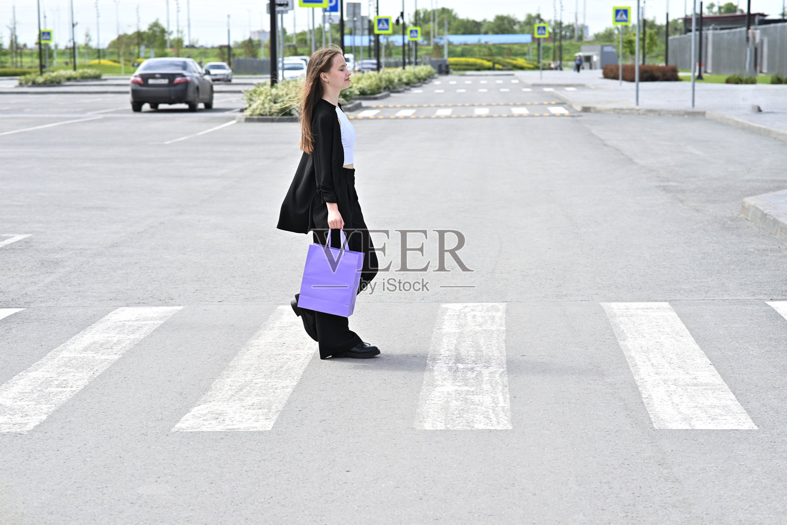 一位女性在住宅区的街道上手持紫色购物袋。照片摄影图片