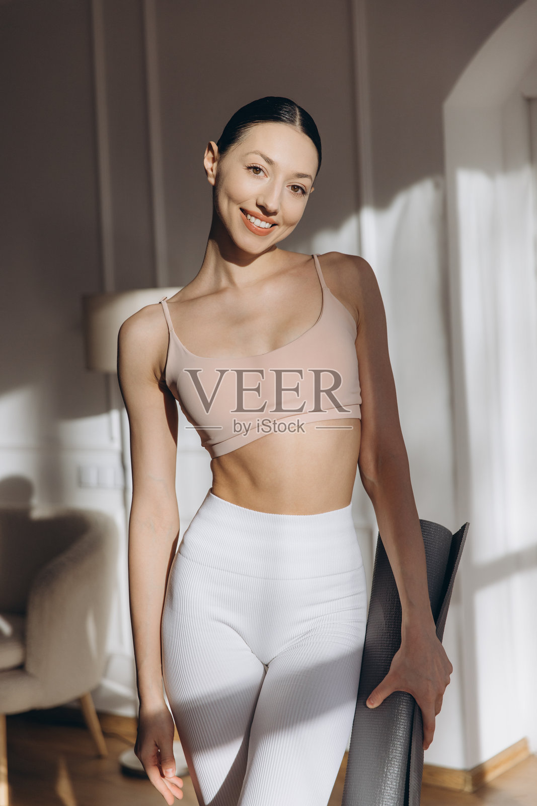 年轻女性手持瑜伽垫，微笑着准备在家锻炼照片摄影图片