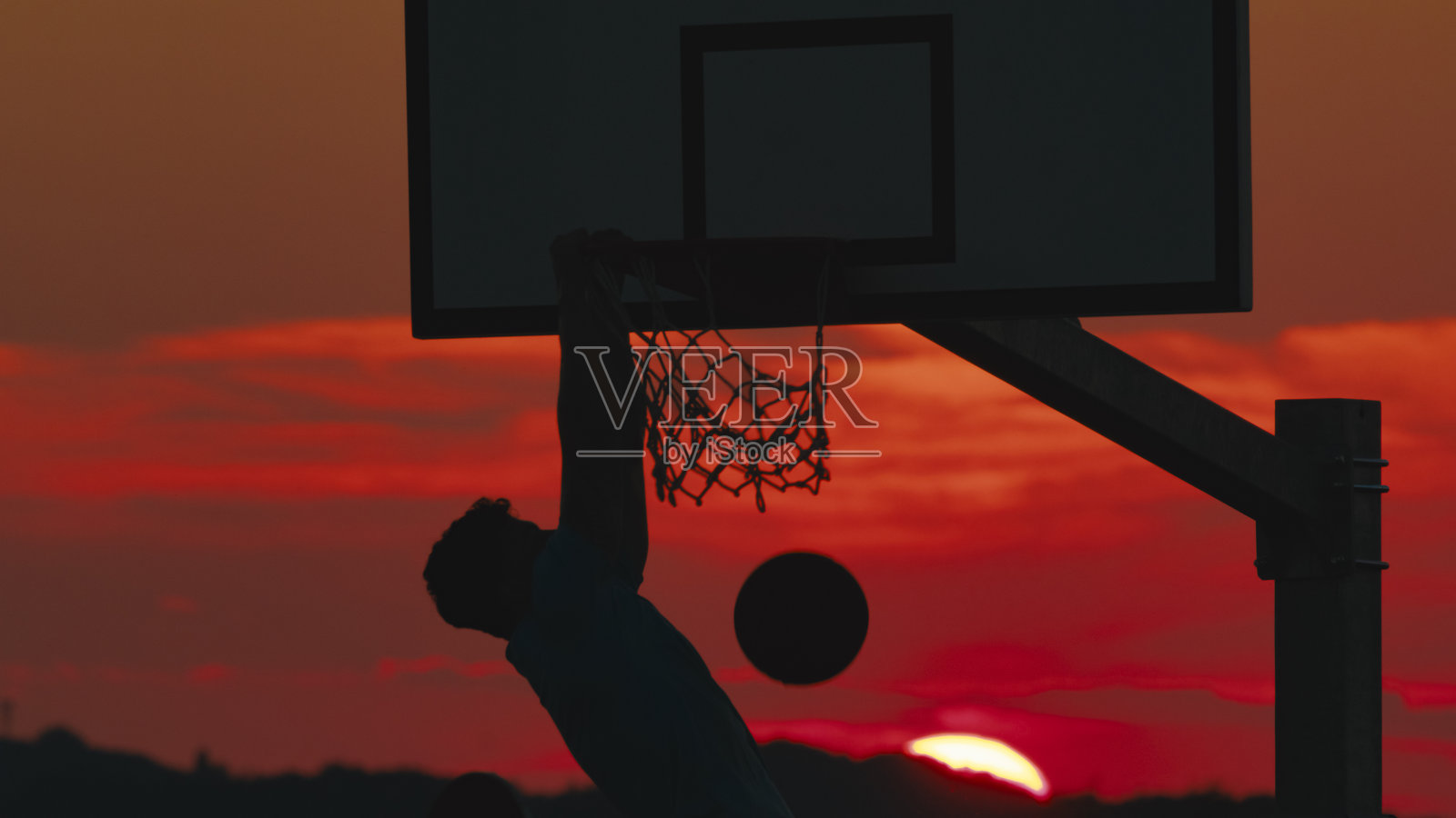 篮球运动员的剪影在强力扣篮后悬挂在篮筐上照片摄影图片