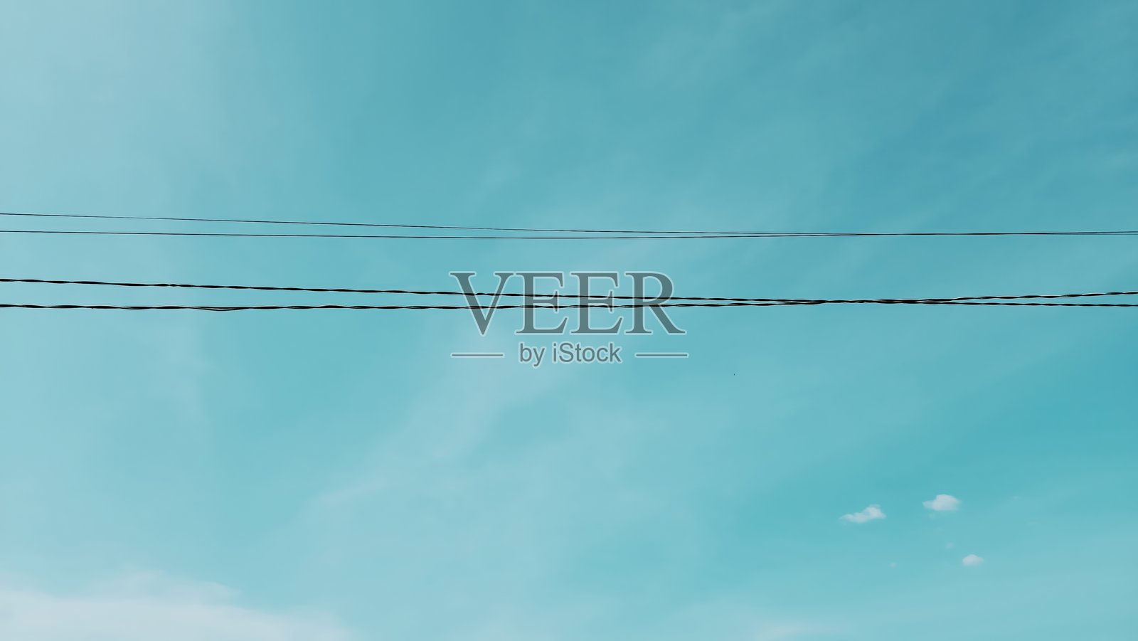 电力线在柔和的蓝绿色天空和轻盈的云朵下照片摄影图片