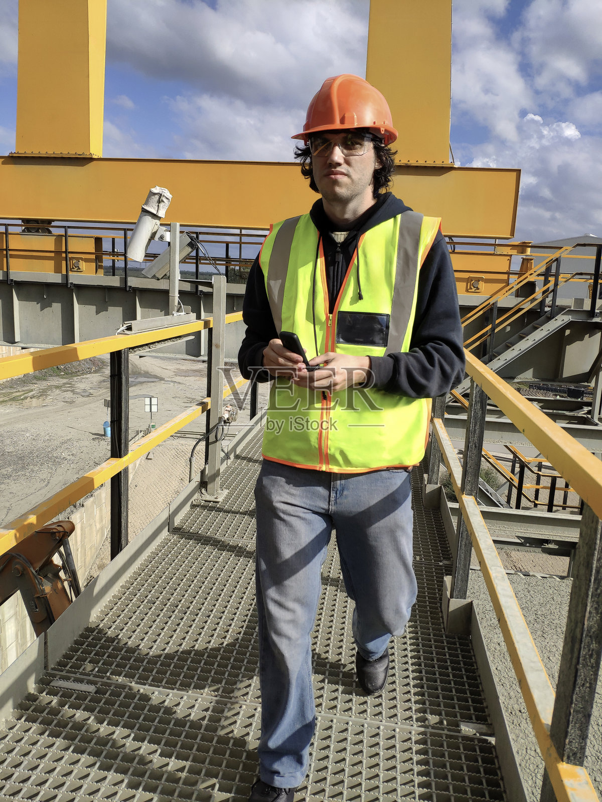 穿着反光背心和安全头盔的工人在工业金属桥上行走照片摄影图片