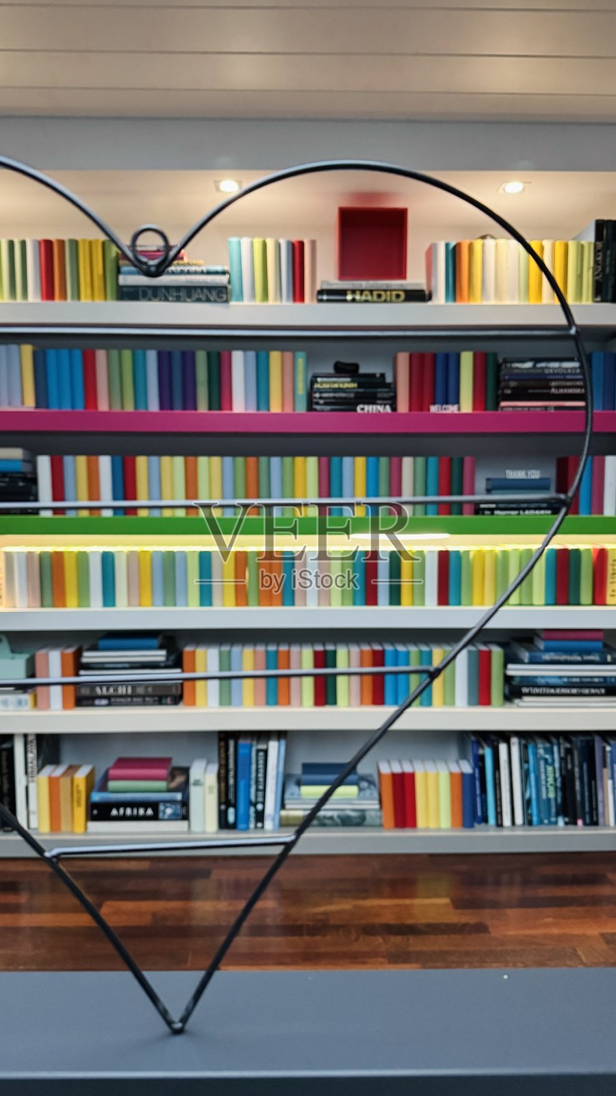 书架上紧密摆满了许多五颜六色的书籍，前景中可见一个心形图案照片摄影图片