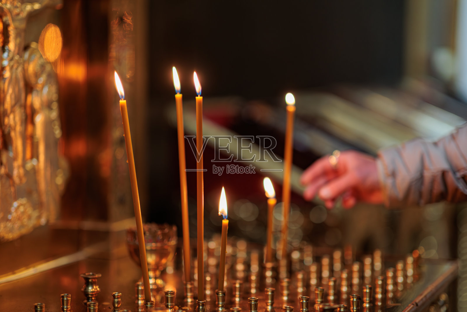 在教堂里点蜡烛的男人。燃烧的蜡烛在十字架和耶稣受难像的背景下，体现了基督教的宗教概念。照片摄影图片