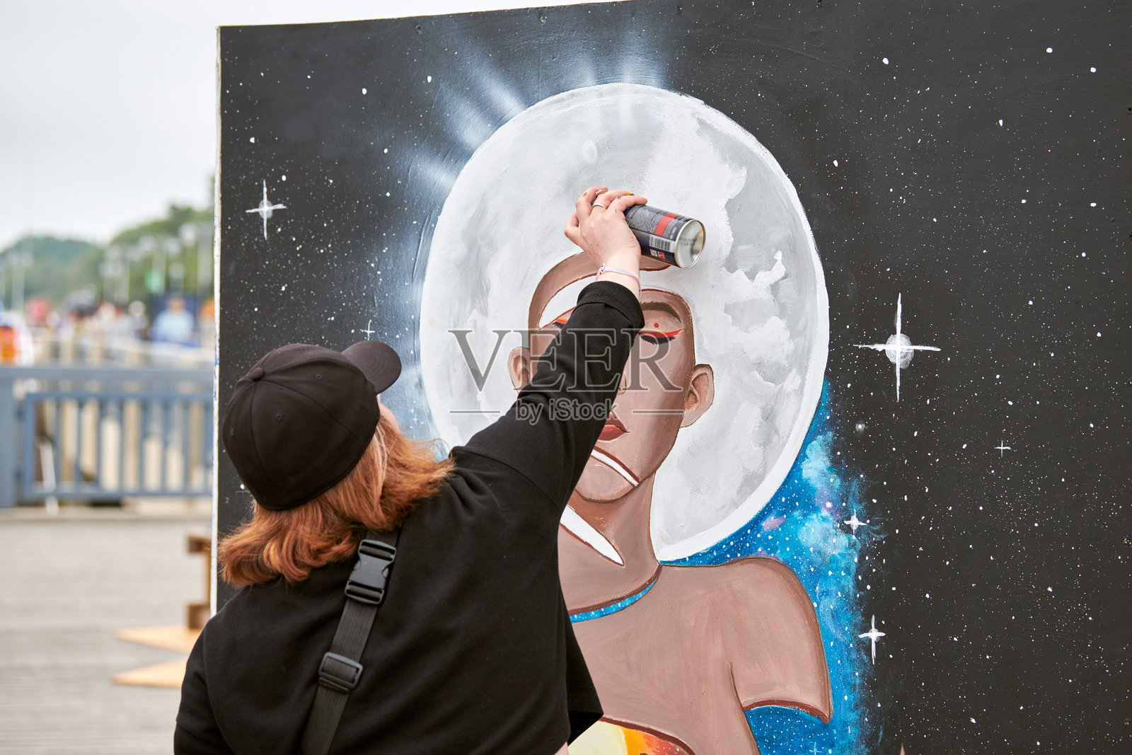 戴黑色帽子的女性艺术家正在用喷漆罐在画布上作画。照片摄影图片