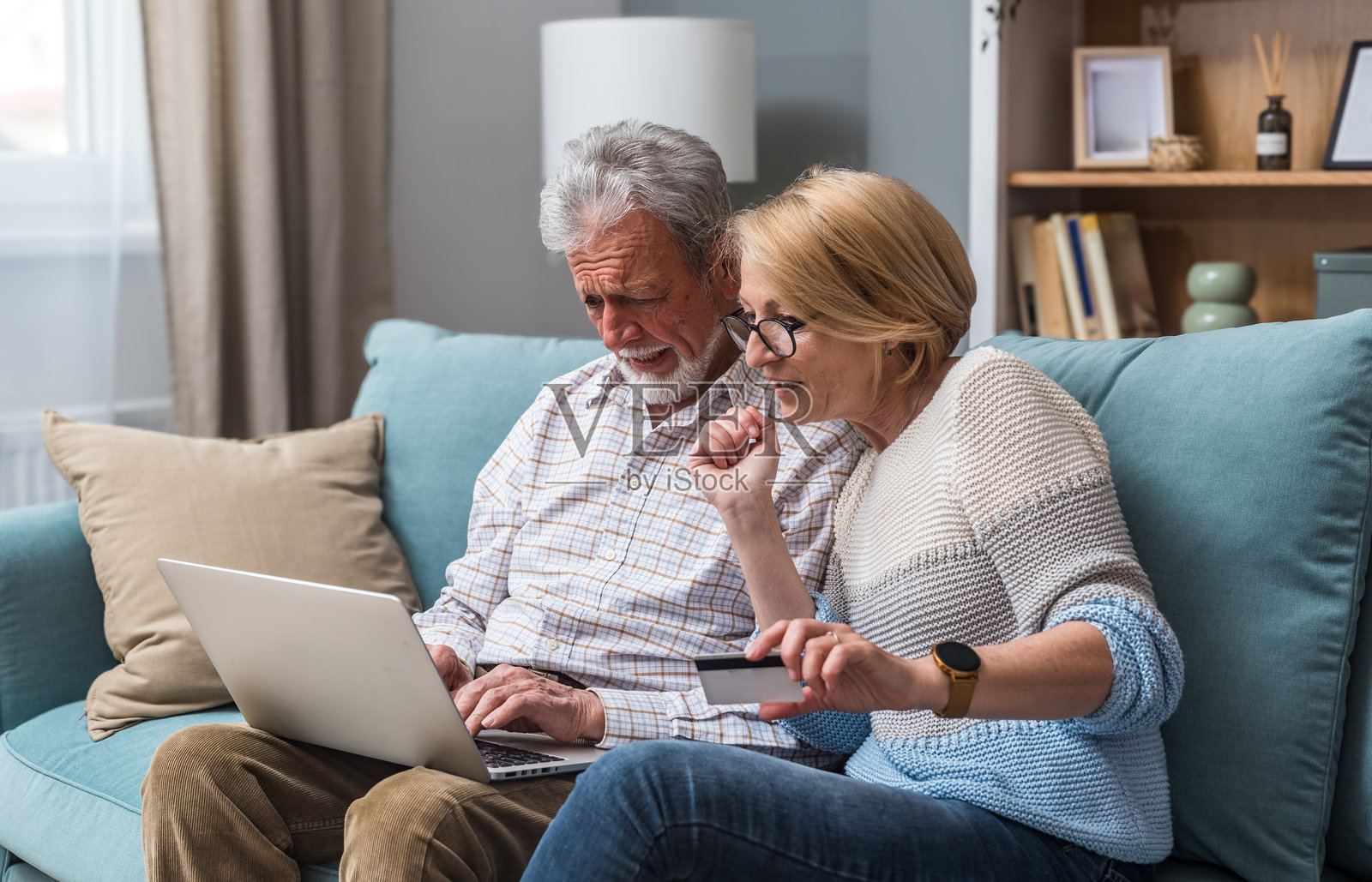 老年夫妇，男士和女士，使用笔记本电脑和信用卡进行在线购物和订购。已婚夫妻在家中沙发上使用互联网和科技。照片摄影图片