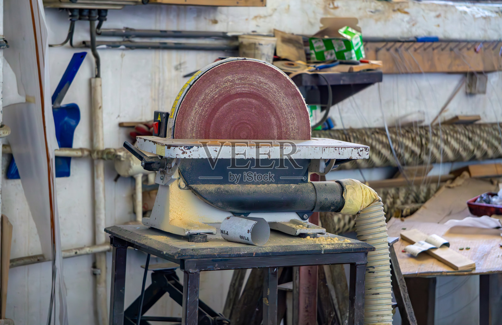一个废弃的木工车间，中央是一台安装在金属桌子上的圆盘砂光机。机器周围可以看到木屑和车间设备的元素。背景是放置工具的架子。照片摄影图片