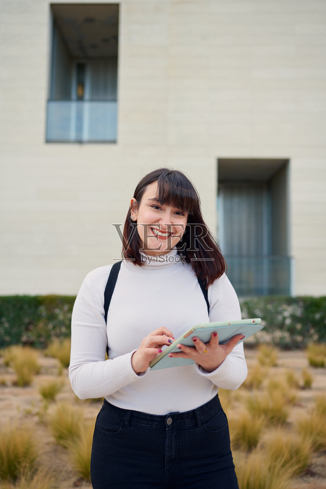 微笑的大学生在学院建筑外使用平板电脑照片摄影图片