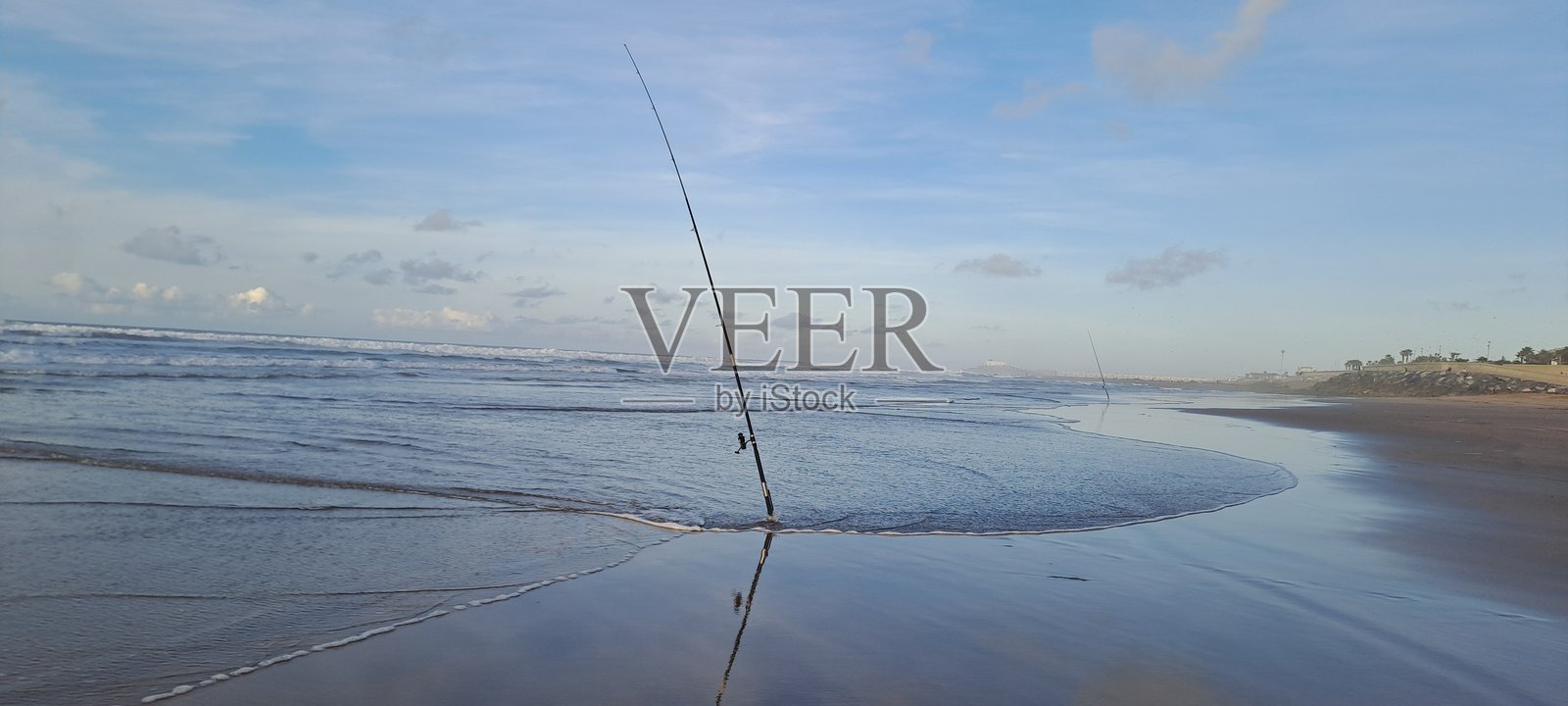 海滩岸边的钓鱼竿倒映在湿沙上照片摄影图片