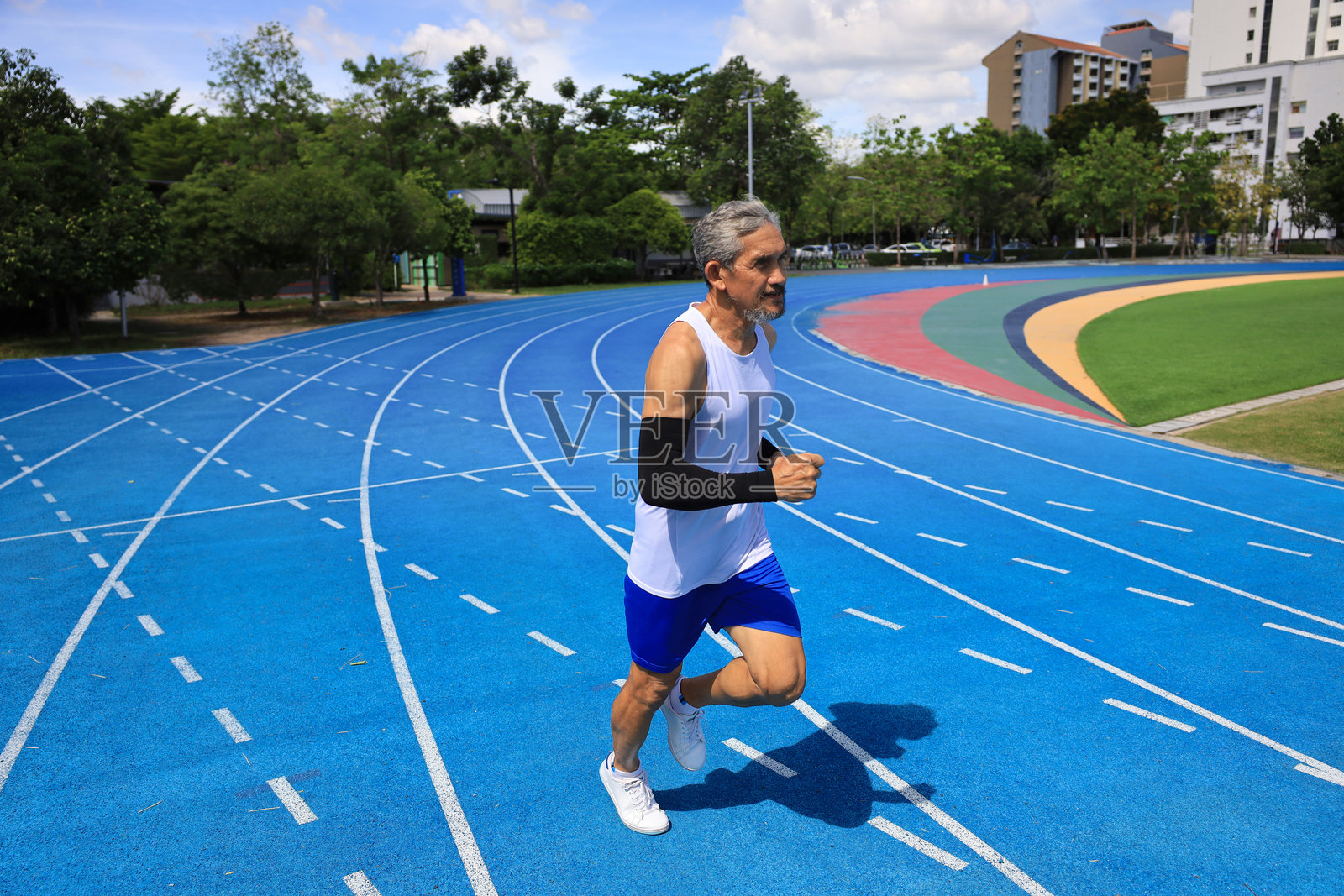 亚洲老年运动员在专业蓝色跑道上练习跑步，进行专业锻炼、体育训练和健康长寿的理念。照片摄影图片