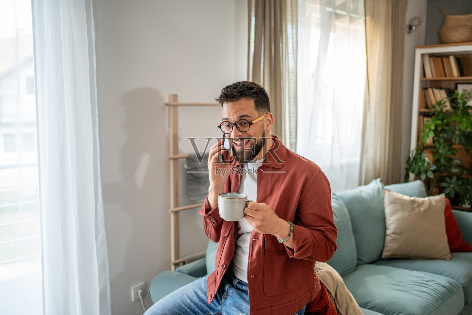 年轻男子在家里一边喝咖啡一边打电话照片摄影图片