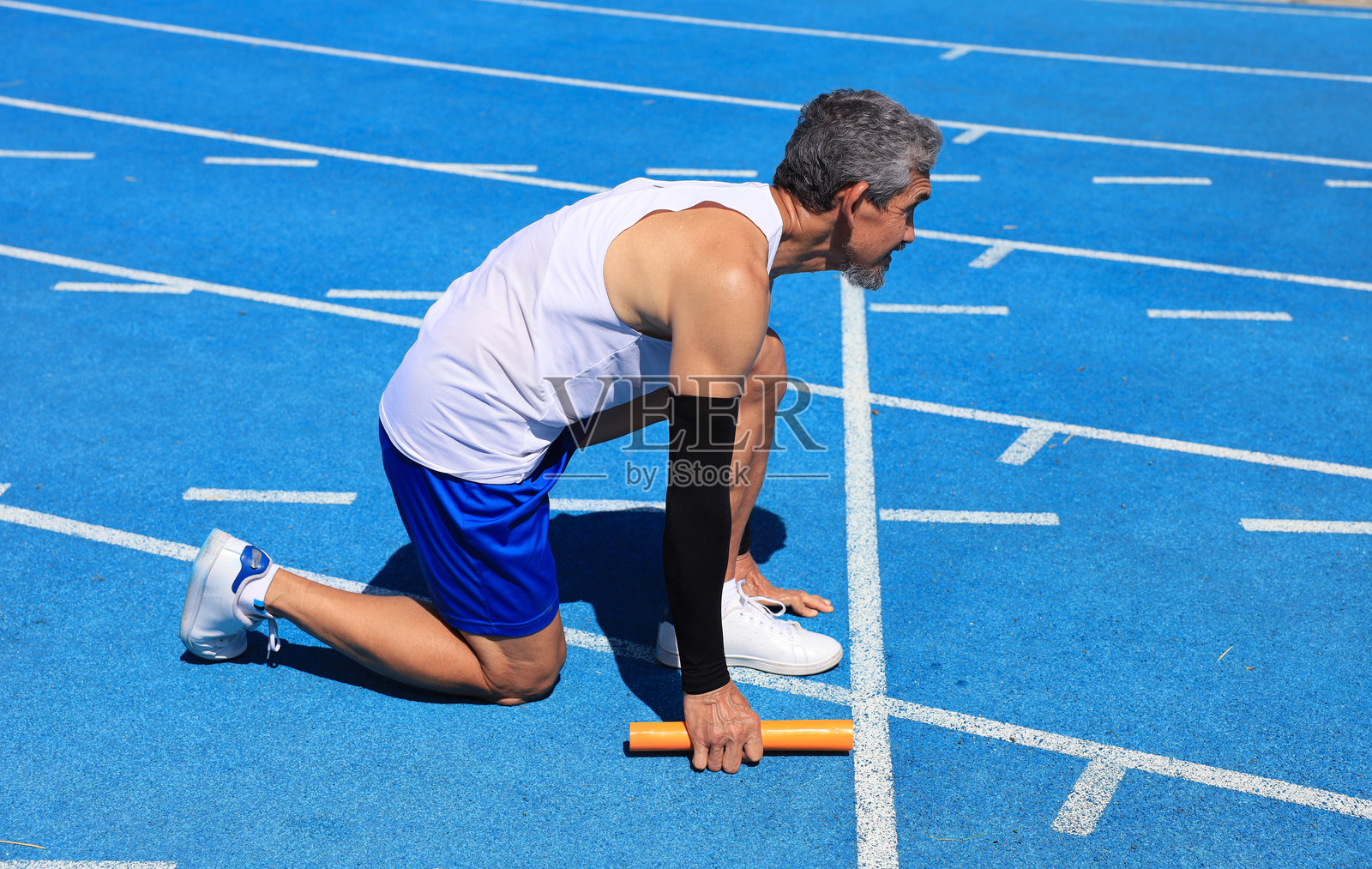 亚洲资深运动员在专业蓝色跑道上练习起跑，进行专业运动训练和健康锻炼，以促进长寿。照片摄影图片