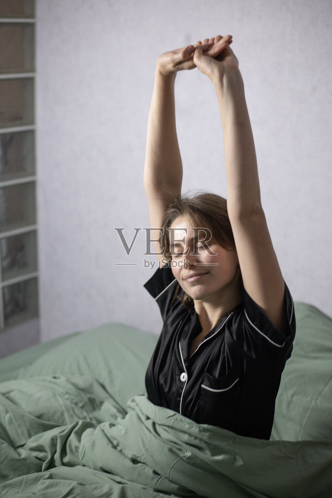 一位女性坐在床上伸展，双臂伸展开来照片摄影图片