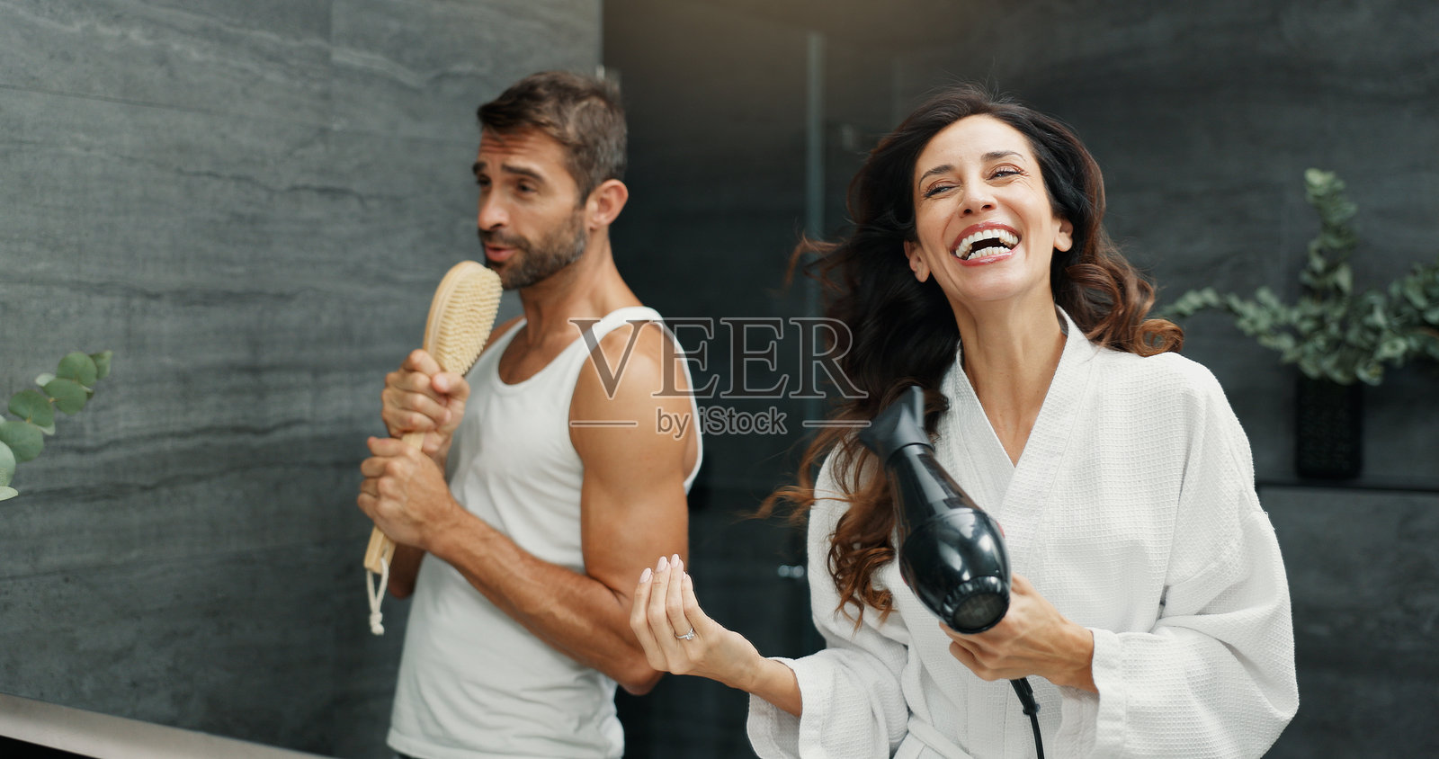 在浴室镜子前唱歌的快乐情侣，享受彼此的陪伴，轻松愉快。爱、婚姻以及男女之间的健康、玩乐关系，适合早晨的日常生活。照片摄影图片