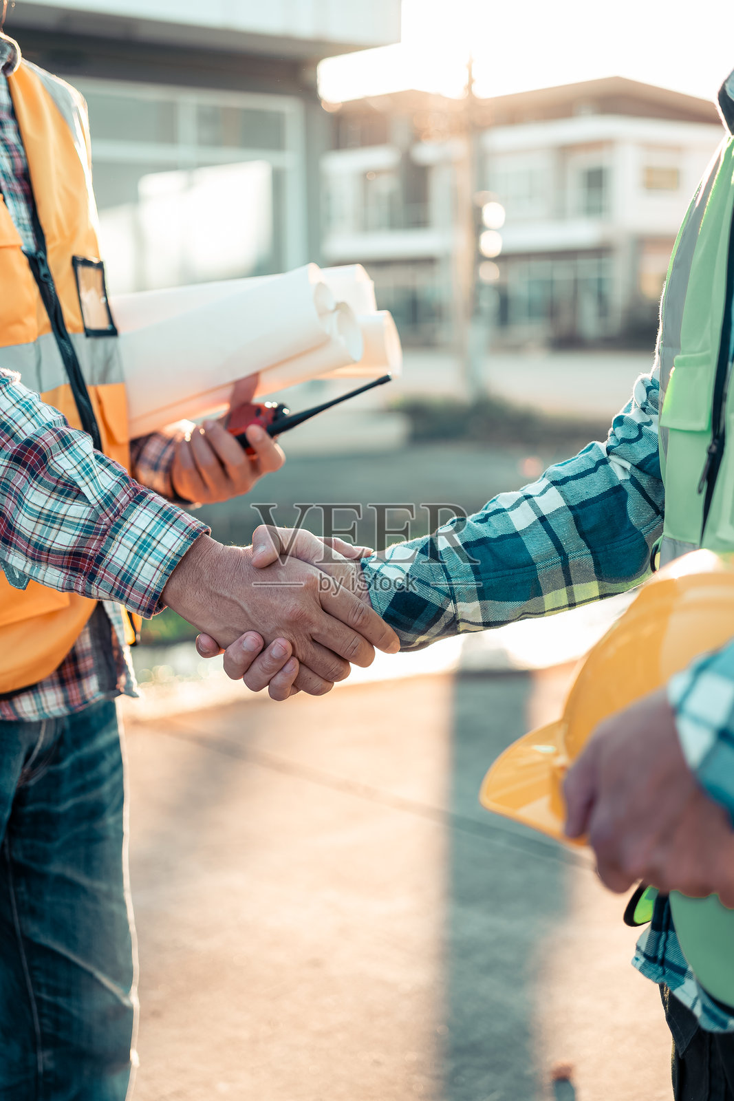 建筑工人和工程师在施工现场握手。男性工程师和承包商团队在施工现场查看蓝图并握手。团队合作概念。照片摄影图片