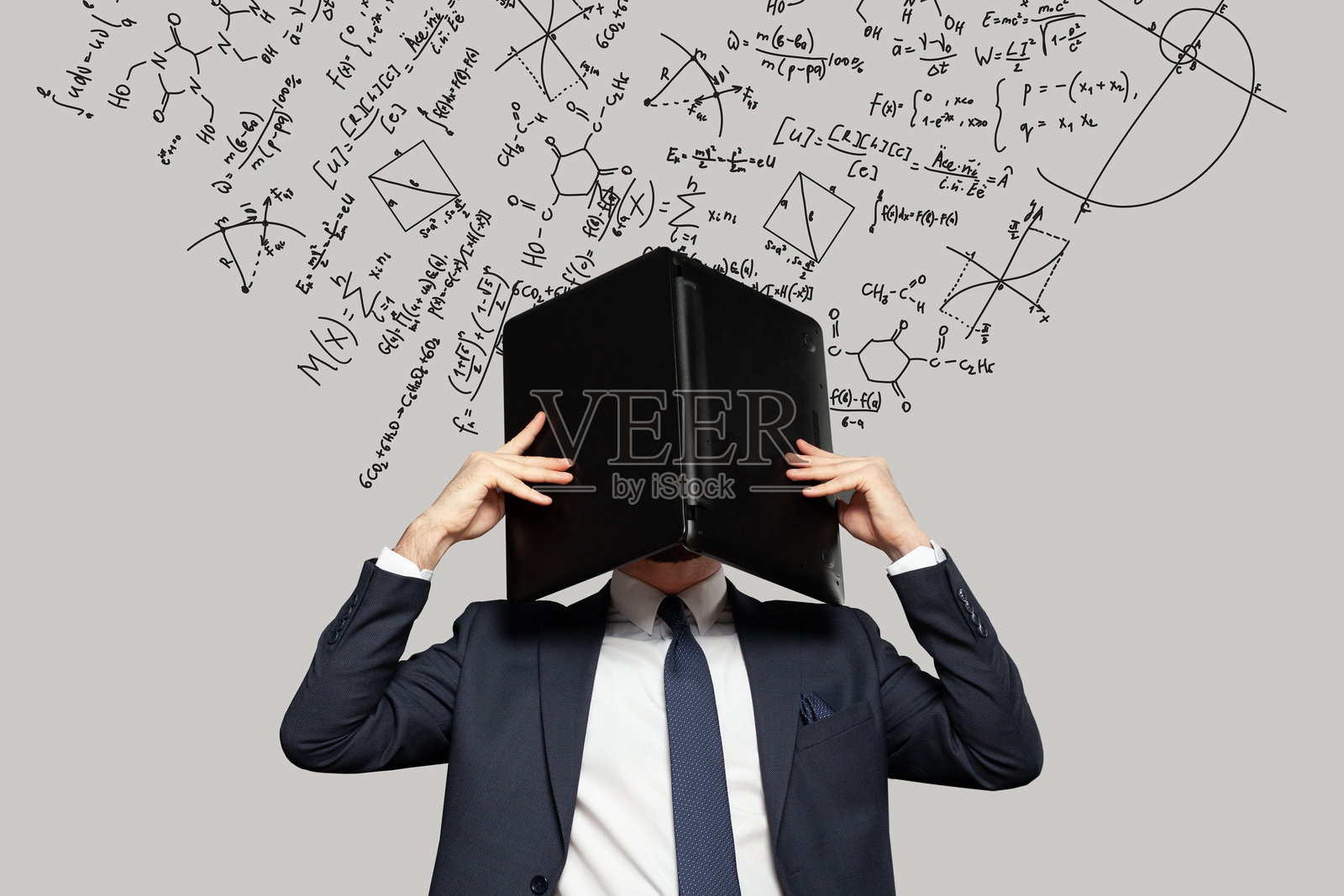 沮丧的压力山大的商人在办公室里把头藏在笔记本电脑下，背景是数学公式。关于金钱、教育和创业的概念。照片摄影图片