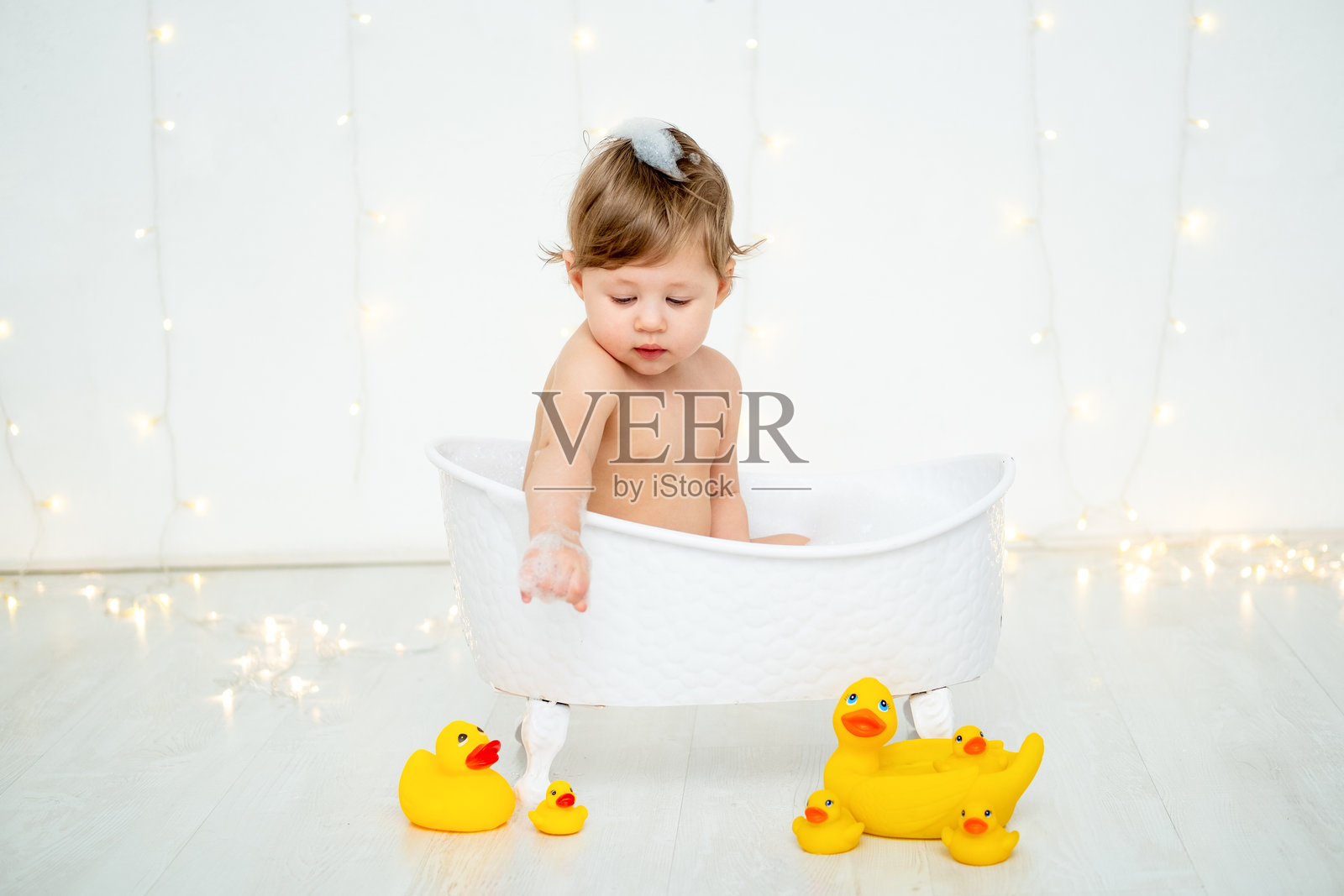 一个小男孩在泡泡浴中洗澡，玩着橡皮鸭，背景为白色孤立，留有文字空间。一个快乐的小孩正在清洗文字区域。照片摄影图片
