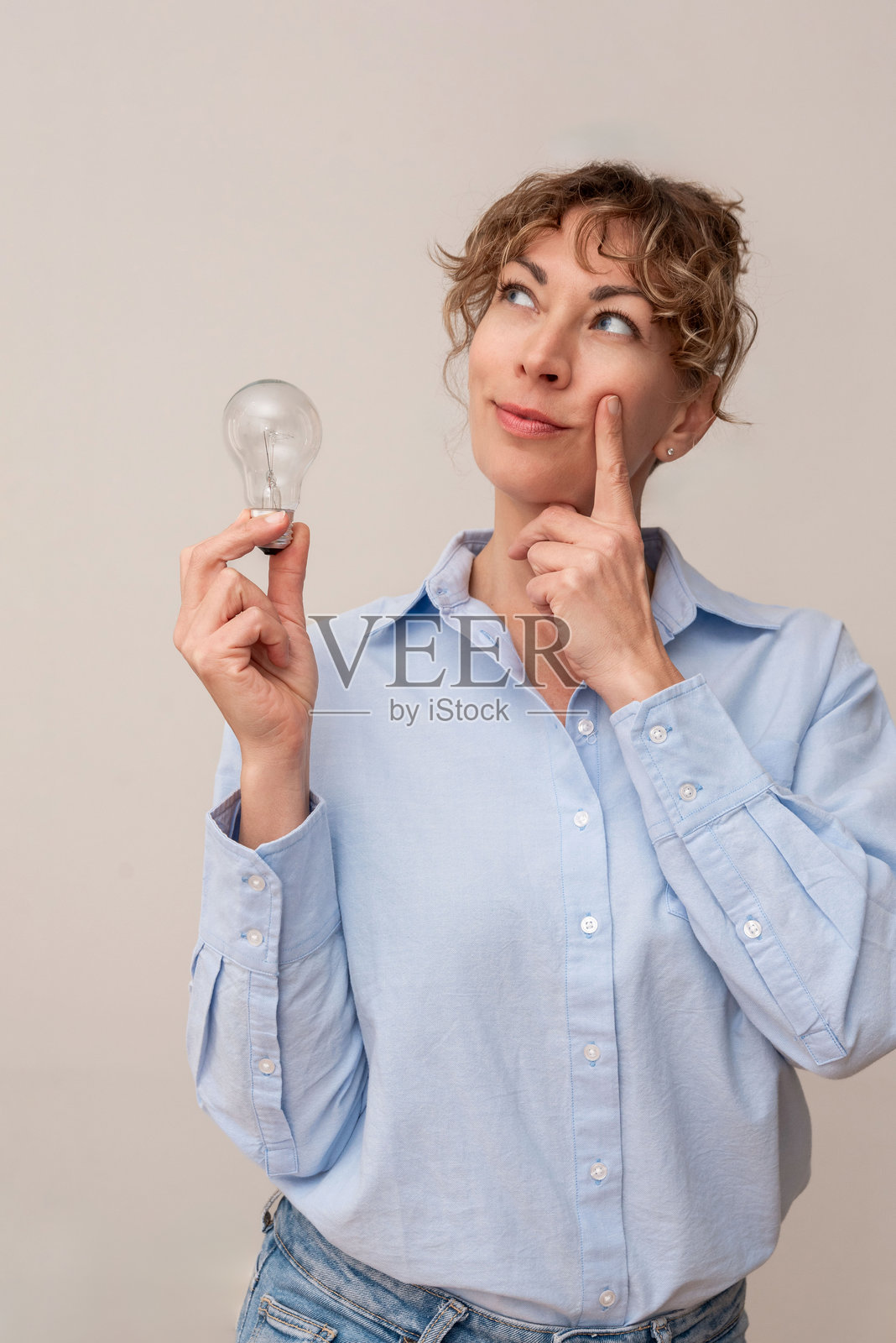 沉思的女性竖版肖像，手握灯泡，思考她创业的创新想法照片摄影图片