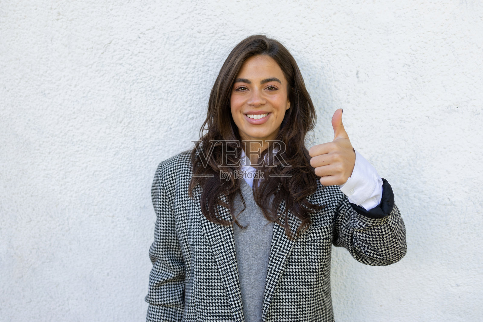 一位愉快的女商人站在白色墙壁前，做出竖起大拇指的手势。照片摄影图片