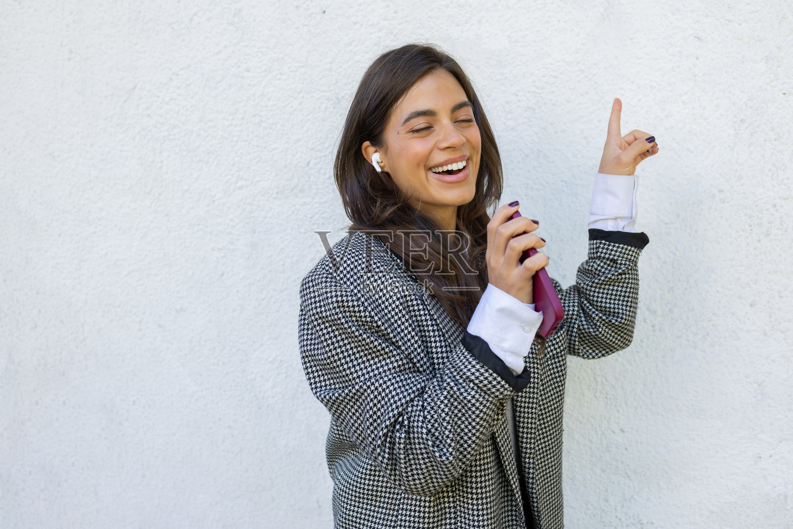 微笑的女商人一边跳舞一边唱歌，佩戴无线耳机，手持智能手机，享受工作间隙。照片摄影图片