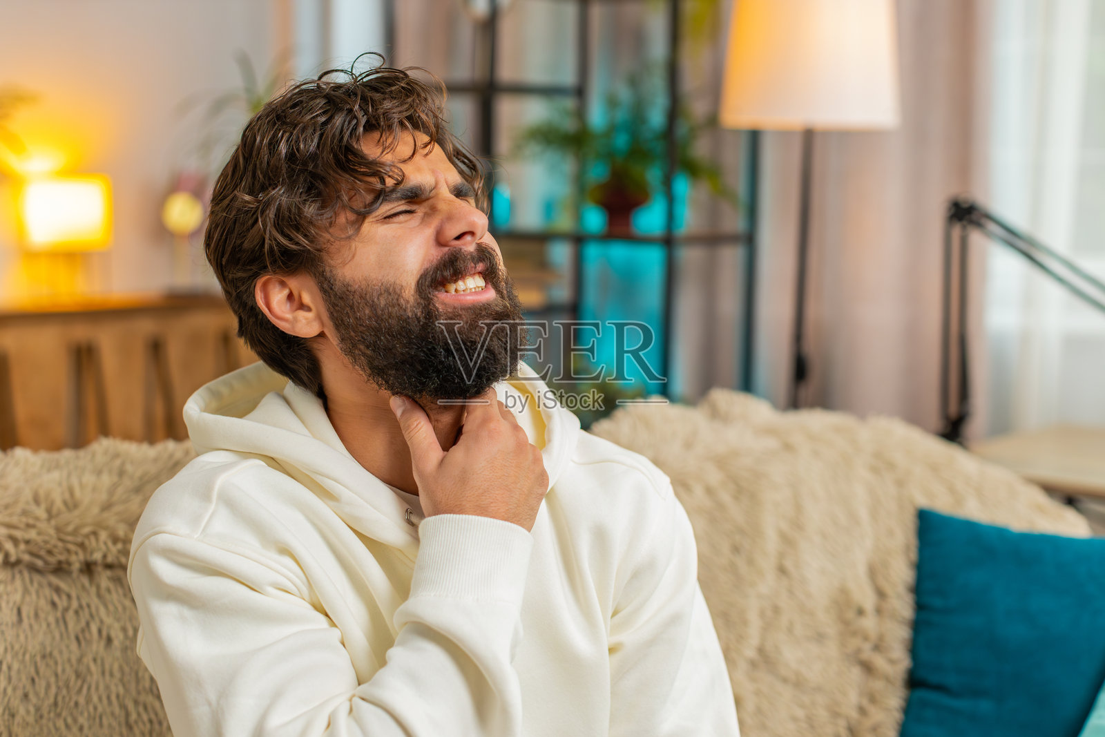 沮丧的印度年轻人用手捂住喉咙，感到喉咙痛和扁桃体发炎。照片摄影图片