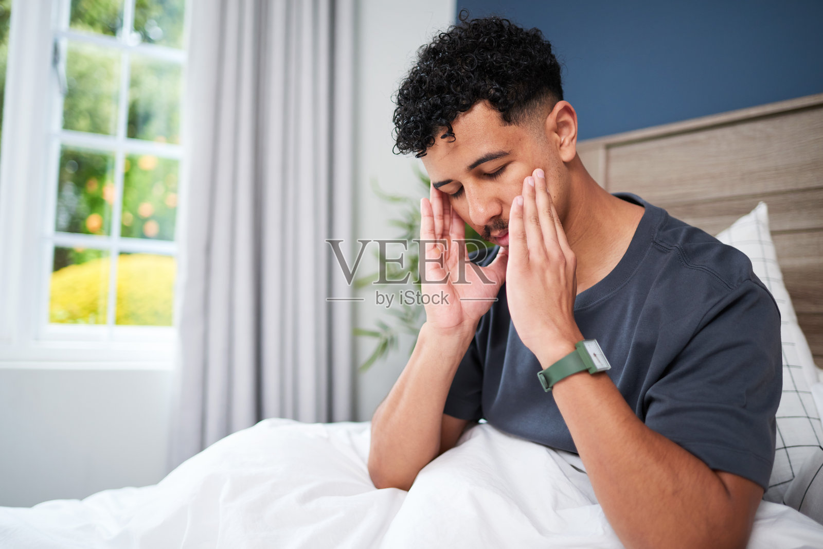 男人坐在床上，双手抱头，显得压力重重或不适。照片摄影图片