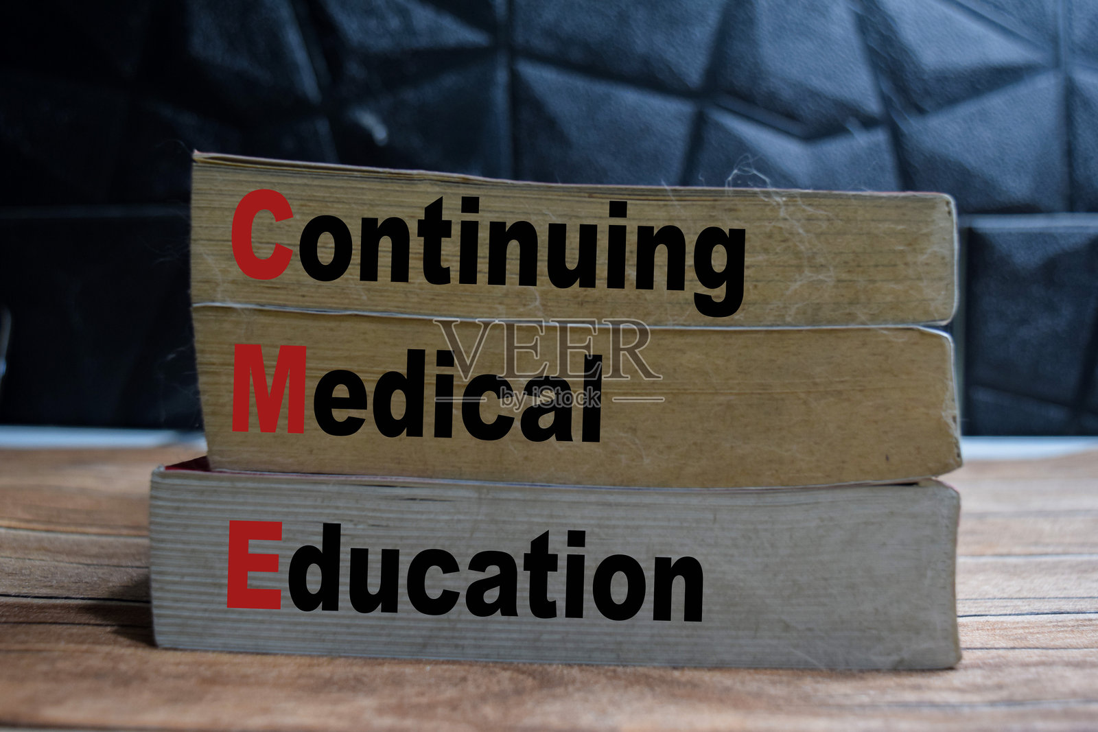 木桌上和黑色背景下的书籍，上面写着“CME - 持续医学教育”照片摄影图片