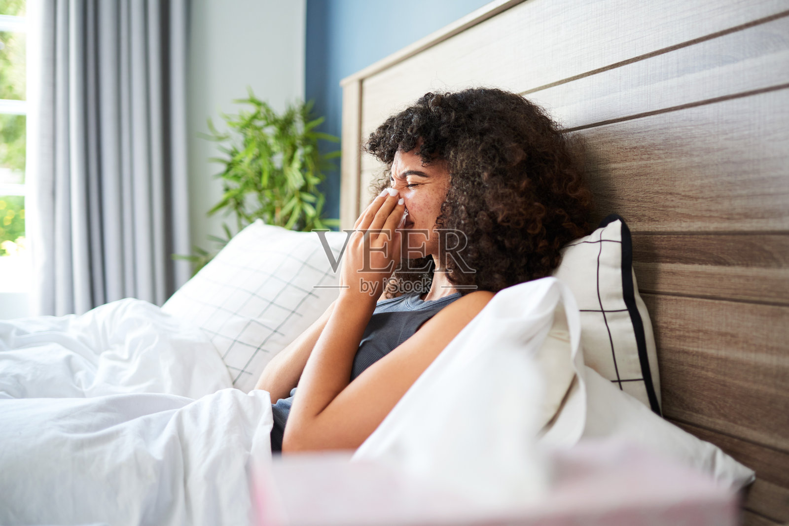 女人在明亮的早晨卧室里打喷嚏，环境轻松舒适照片摄影图片