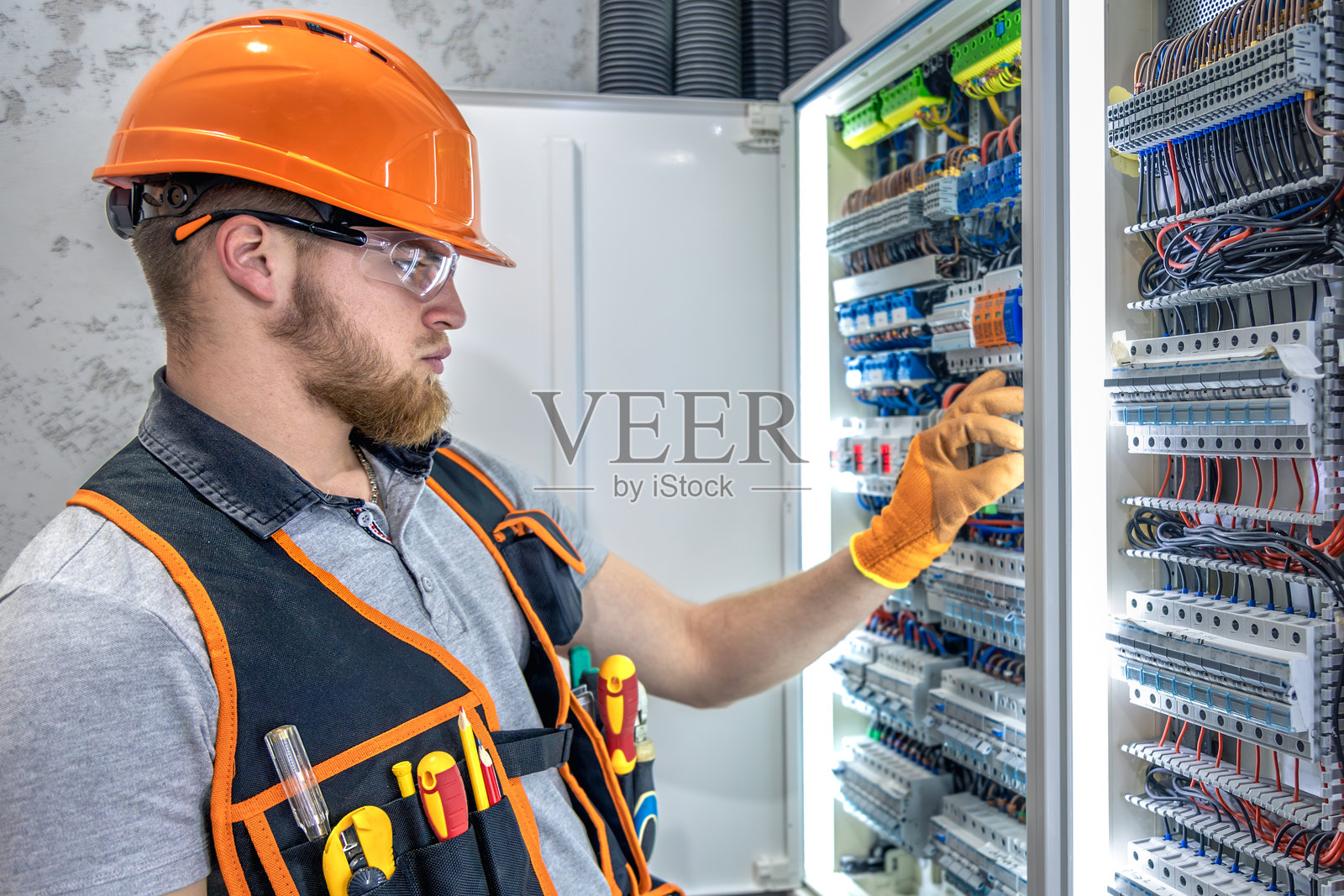 男性电工在电气面板工作。穿着工装的男性电工。照片摄影图片