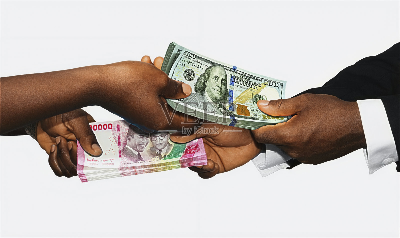 两位非洲黑人用手握住并交换印尼卢比和美元的钞票，背景为白色。配对、称重和比较两国货币。汇率概念。照片摄影图片