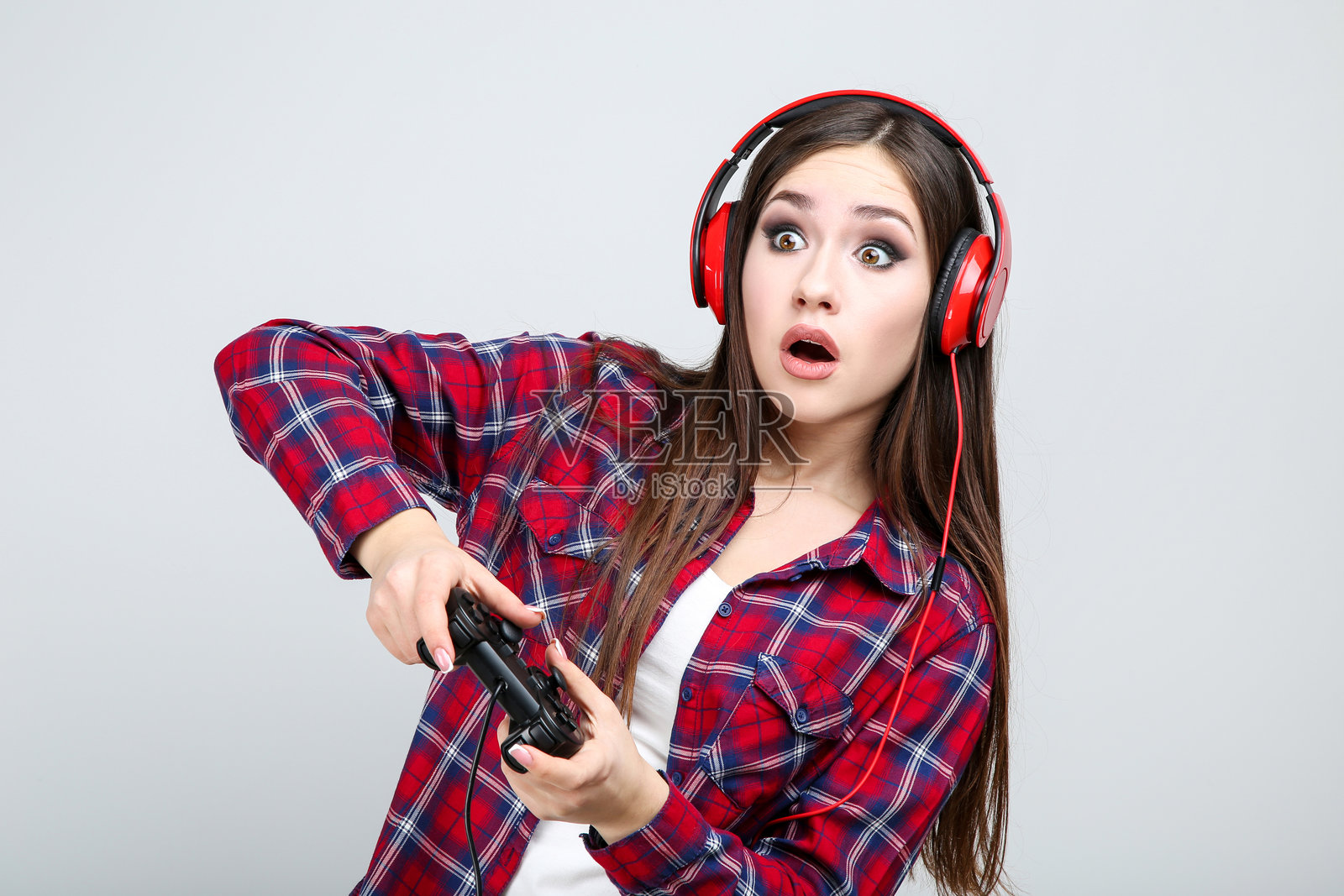 美丽女孩佩戴着耳机，手握操纵杆，背景为灰色。照片摄影图片