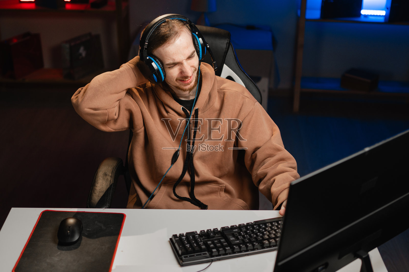 悲伤、沉思的游戏玩家戴着耳机，抓着头，夜晚在霓虹灯下玩在线视频游戏。在家游戏。在线多人锦标赛。电子竞技直播游戏。照片摄影图片