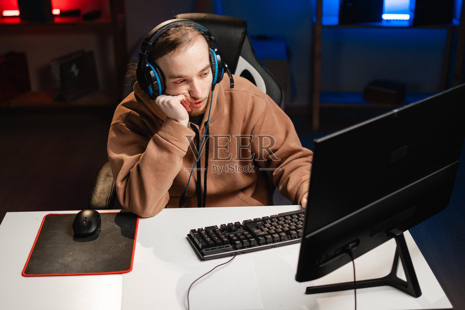 疲惫的游戏玩家在直播中深思，手托着下巴，专注于虚拟挑战，同时与观众互动，进行紧张的游戏环节。照片摄影图片