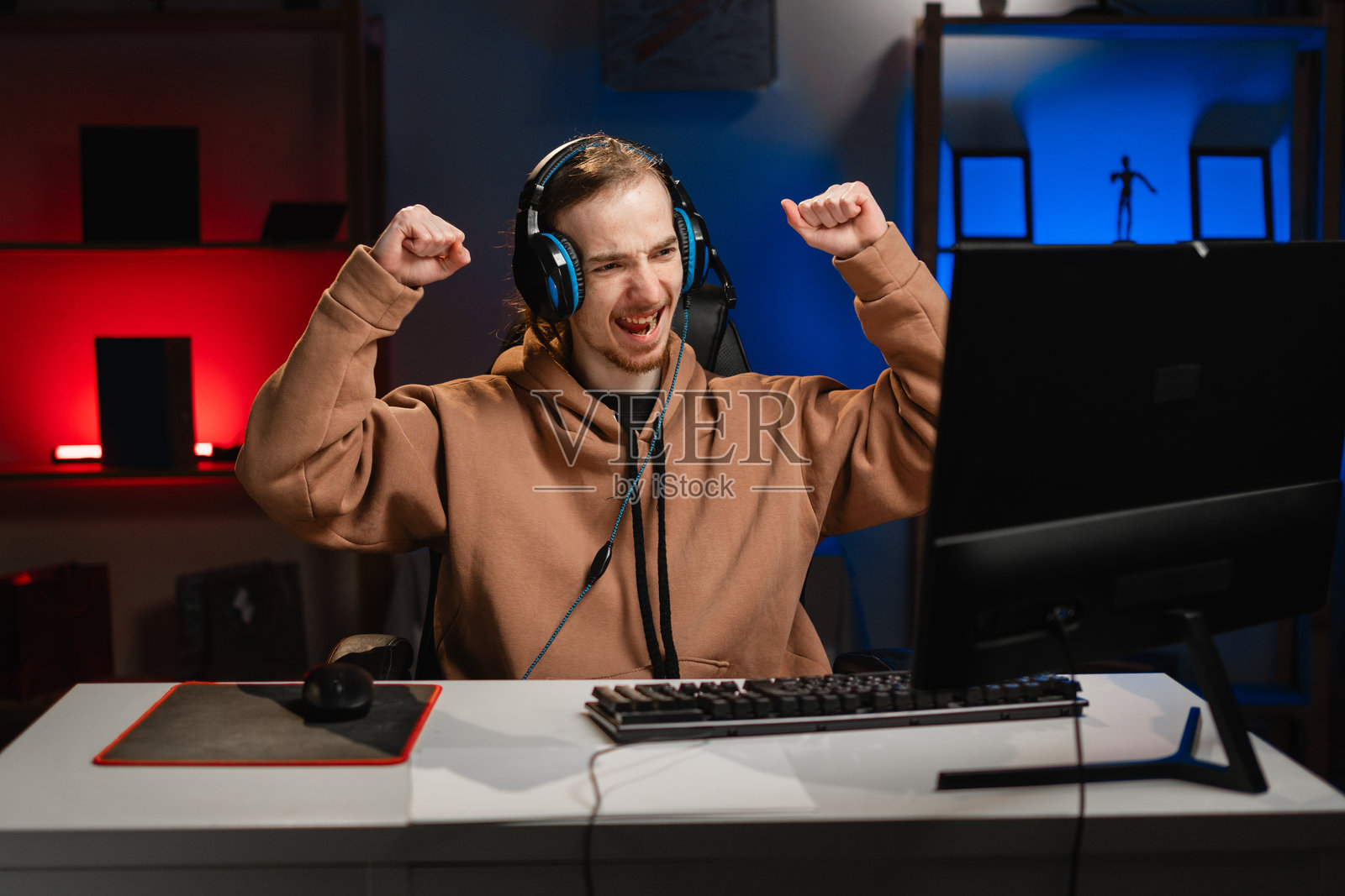 戴着耳机的男性玩家在夜晚的霓虹灯下庆祝胜利，情绪高涨，正在玩在线视频游戏。在家游戏。在线多人锦标赛。电子竞技直播游戏。照片摄影图片