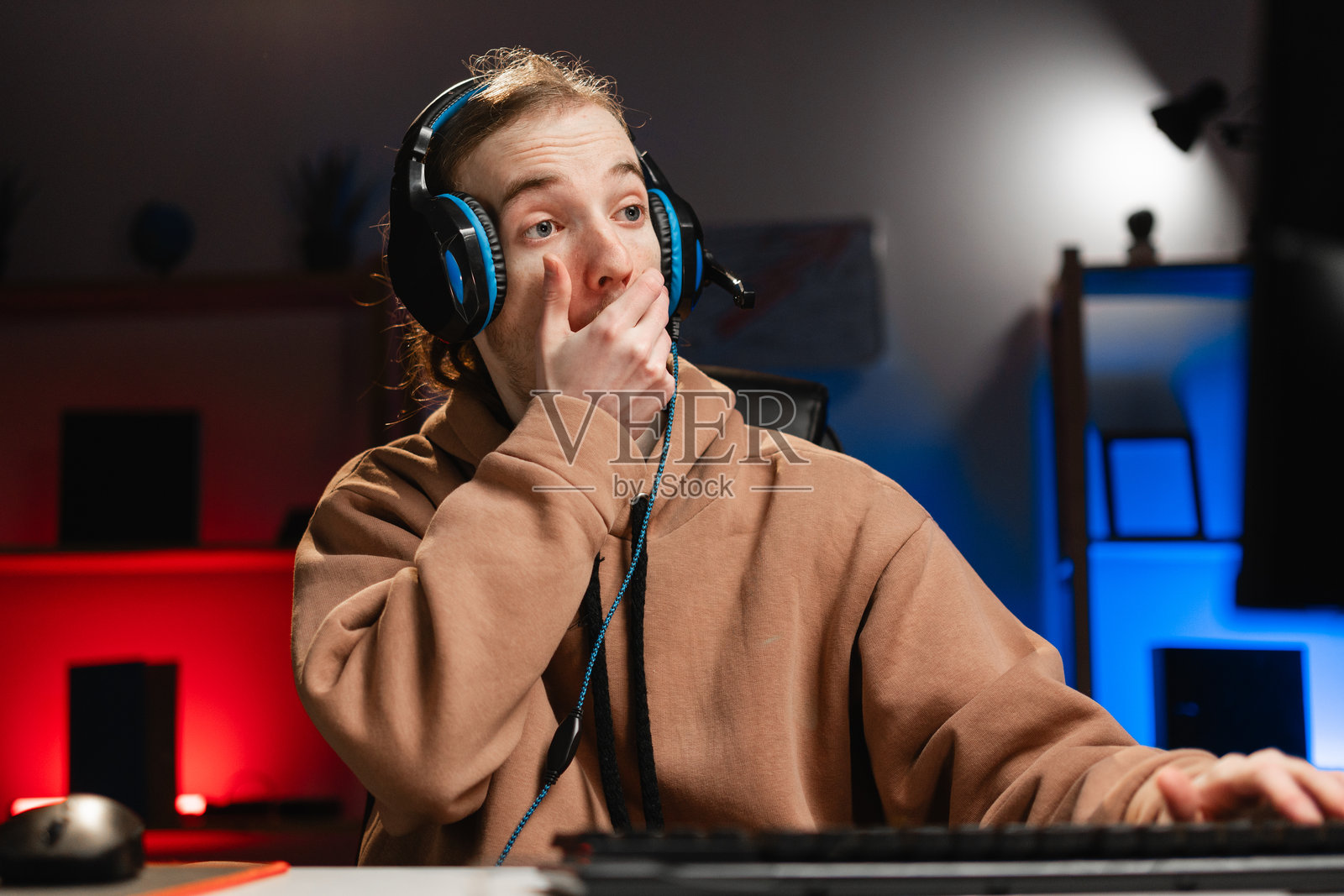 震惊的玩家在夜晚的客厅里玩电脑游戏，惊讶地捂住嘴巴。游戏和电子竞技训练照片摄影图片