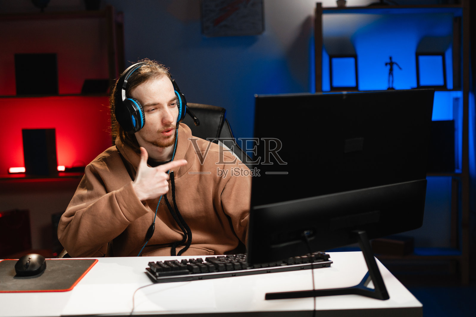 戴着耳机的男性玩家在夜晚的霓虹灯下做出手枪手势，在线玩视频游戏。在家游戏。在线多人锦标赛。电子竞技直播游戏。照片摄影图片