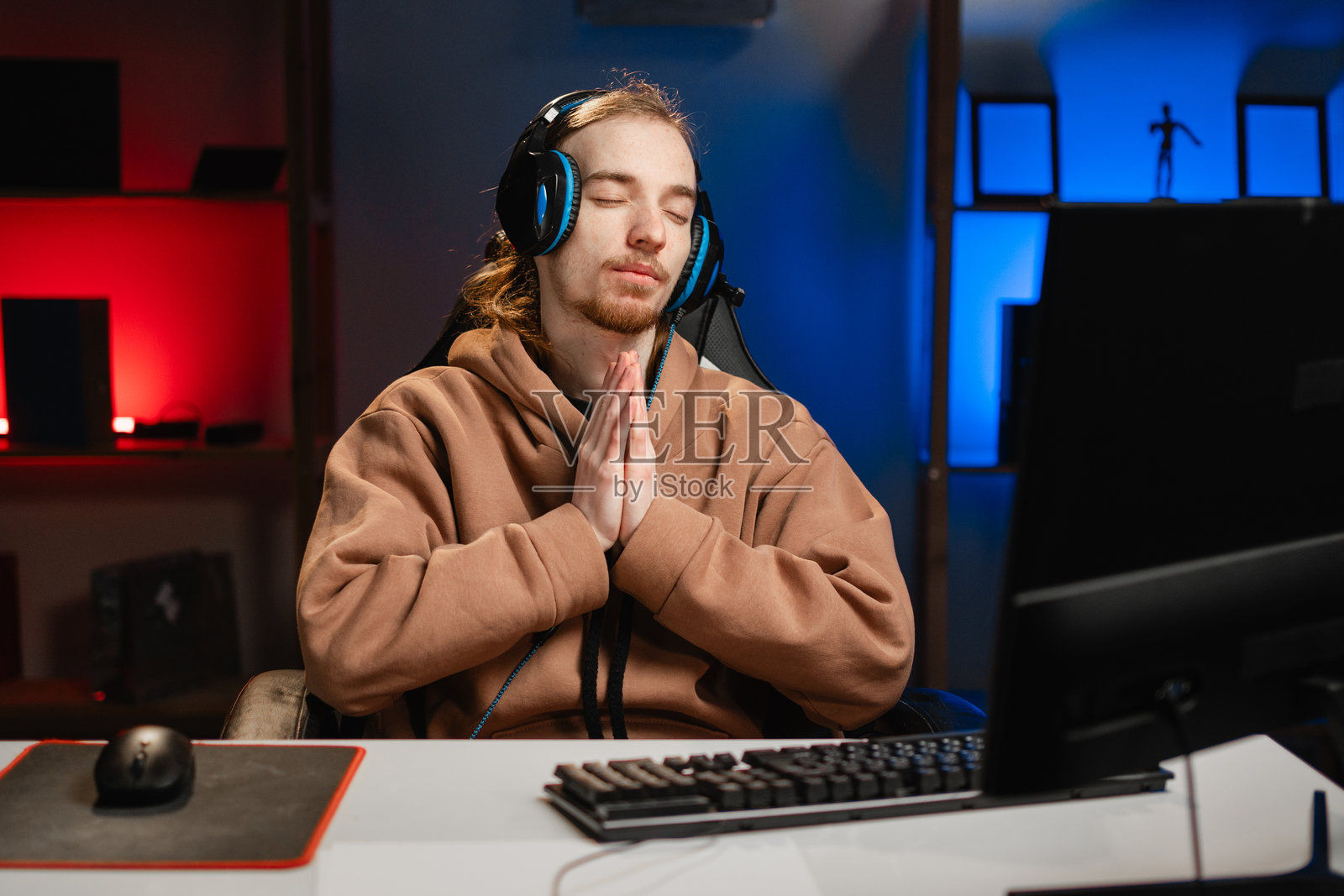 戴着耳机的男性玩家在玩视频游戏，双手合十祈祷，向上帝请求宽恕。照片摄影图片