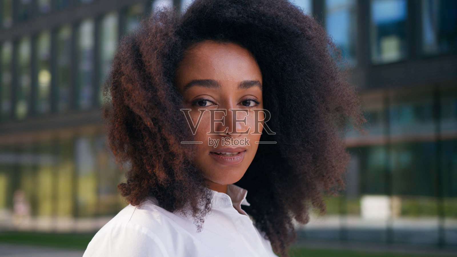 友好的非裔美国女性商人学生在城市户外触摸卷发的肖像，面带微笑，注视着镜头。照片摄影图片