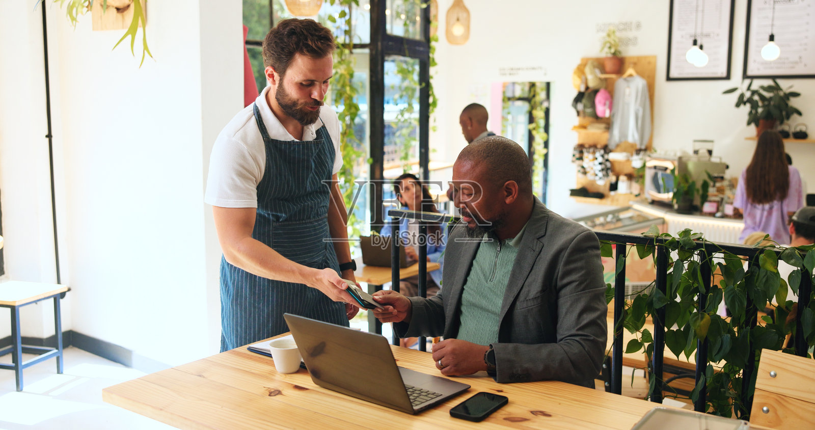 咖啡馆里的男性与笔记本电脑、支付卡，提供酒店服务和便捷的远程工作信用。银行、服务员和顾客在咖啡店使用POS机进行无现金交易的小型企业。照片摄影图片