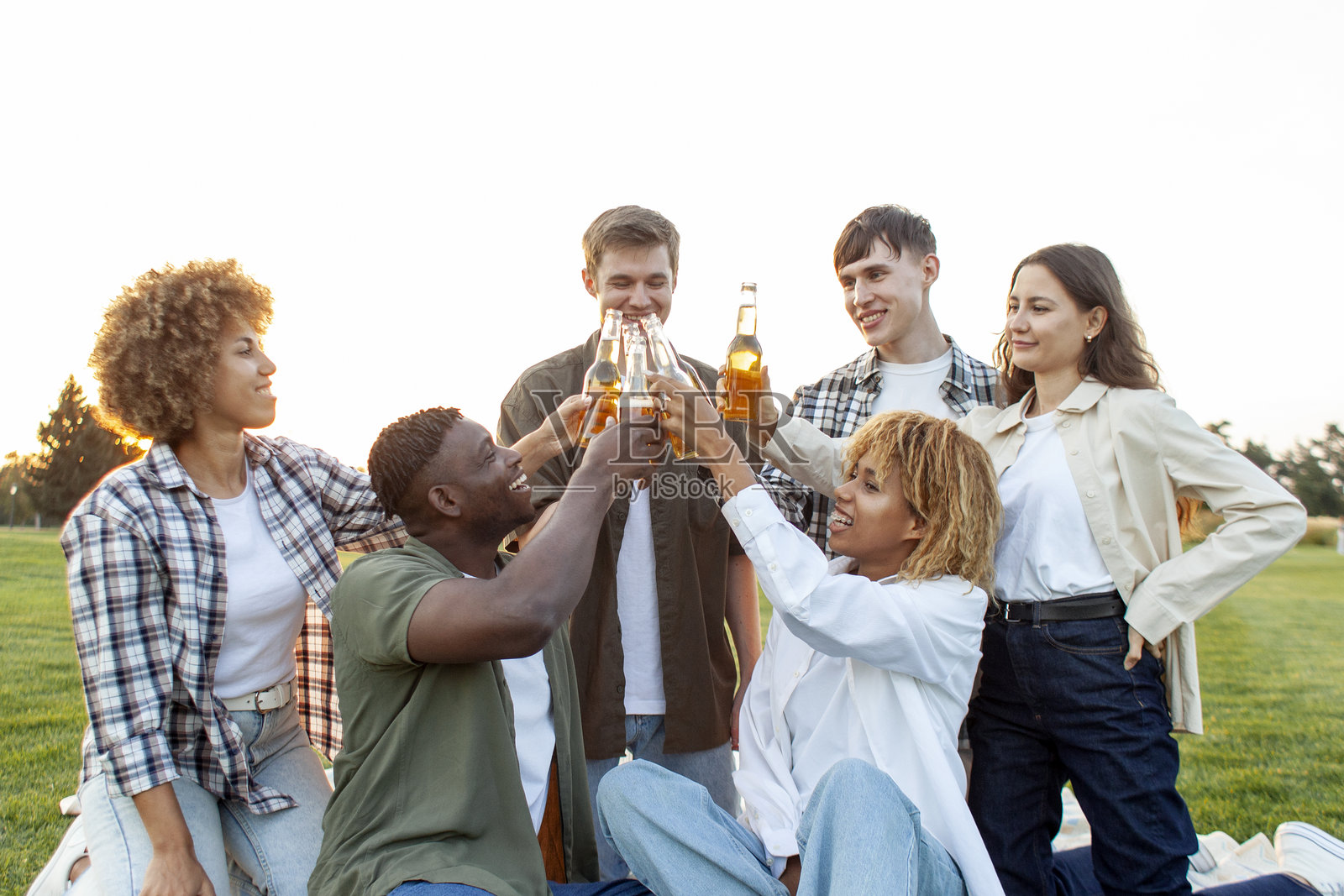 一群不同种族的人在公园放松，庆祝时碰杯并在户外举起啤酒瓶。照片摄影图片