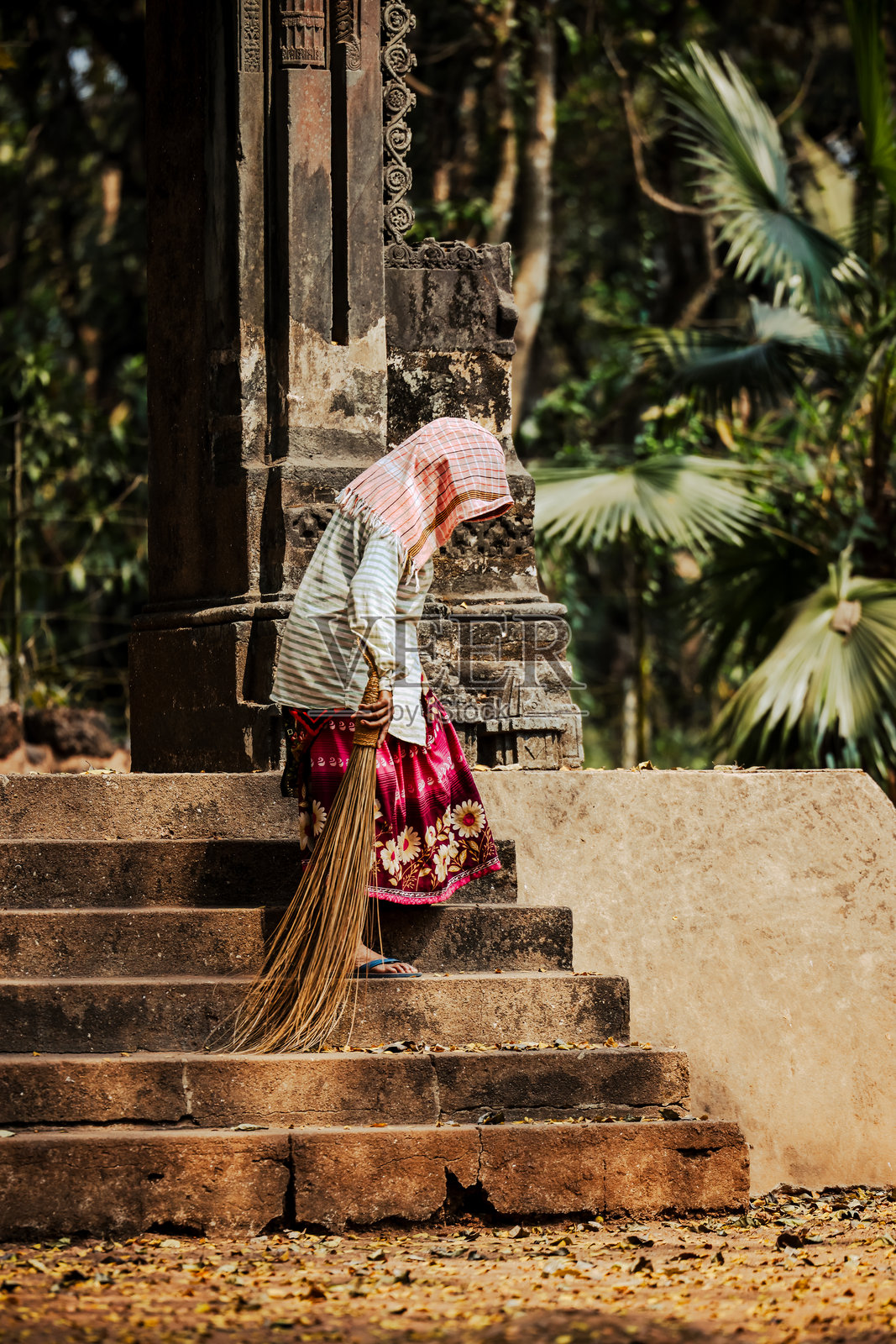 一位女性在印度果阿的圣凯特贾教堂外的阿迪尔肖宫门口扫落叶，圣凯特贾教堂是一座17世纪的天主教教堂。照片摄影图片