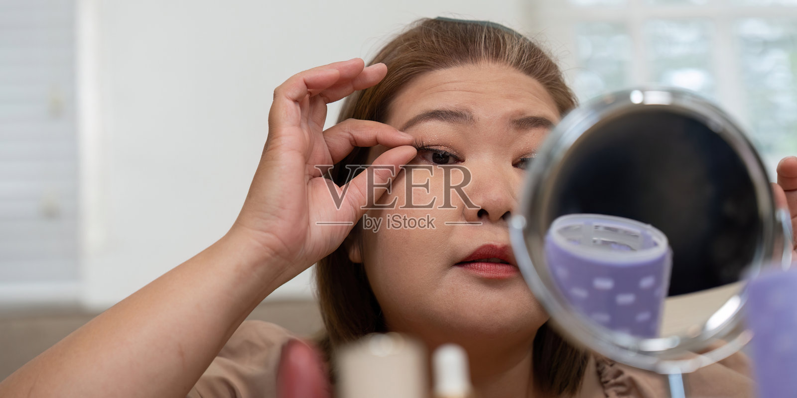 眼妆与精致。一位女性在镜子前涂抹假睫毛，专注于她的眼妆。照片摄影图片